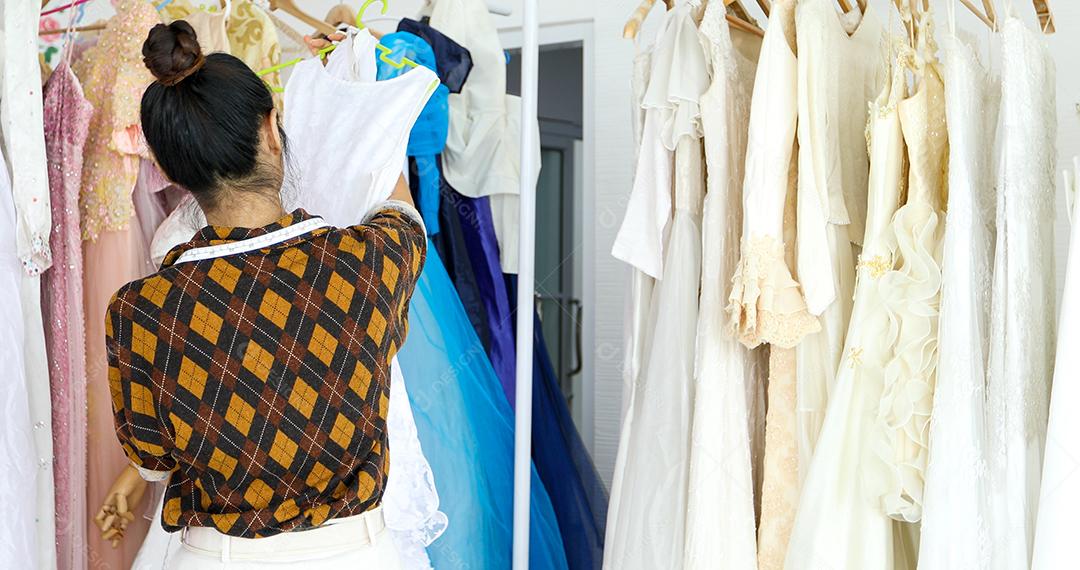 Pequenas Empresas de Mulheres Asiáticas Designer de Moda Trabalhando e usando smartphone e tablet com vestidos de noiva na loja de roupas