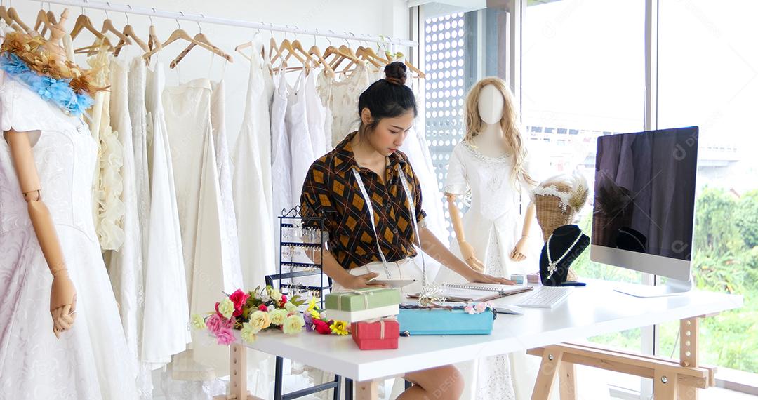 Pequenas Empresas de Mulheres Asiáticas Designer de Moda Trabalhando e usando smartphone e tablet com vestidos de noiva na loja de roupas