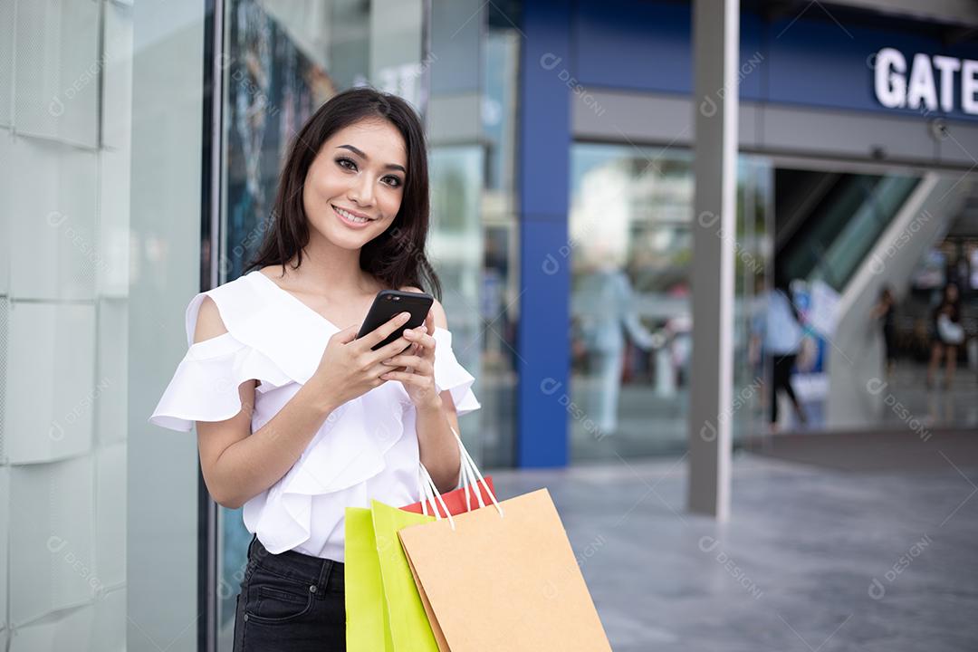 Mulheres asiáticas e linda garota estão segurando sacolas de compras e usando um telefone inteligente e sorrindo enquanto fazem compras no supermercado/shopping