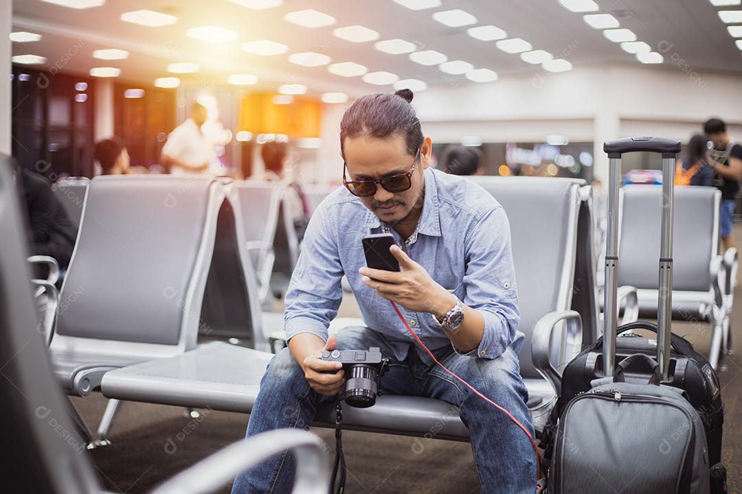 Homem asiático com viajante de mochila usando o telefone celular inteligente para chamada de vídeo e levando em um aeroporto, foco embaçado e suave