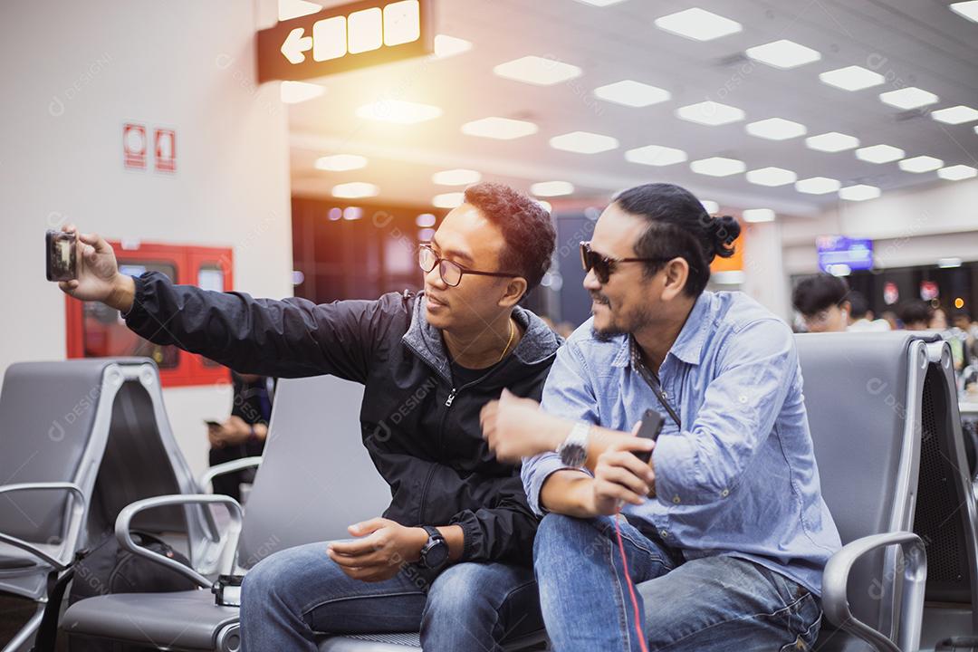 Homem asiático com viajante de mochila usando o telefone celular inteligente para chamada de vídeo e tirando foto em um aeroporto, Foco embaçado e suave