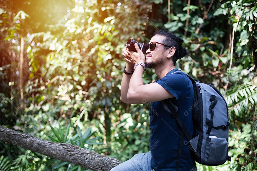 Mochilas de homens asiáticos e viajantes caminhando juntos e felizes estão tirando fotos na floresta, relaxe o tempo em viagens de conceito de férias