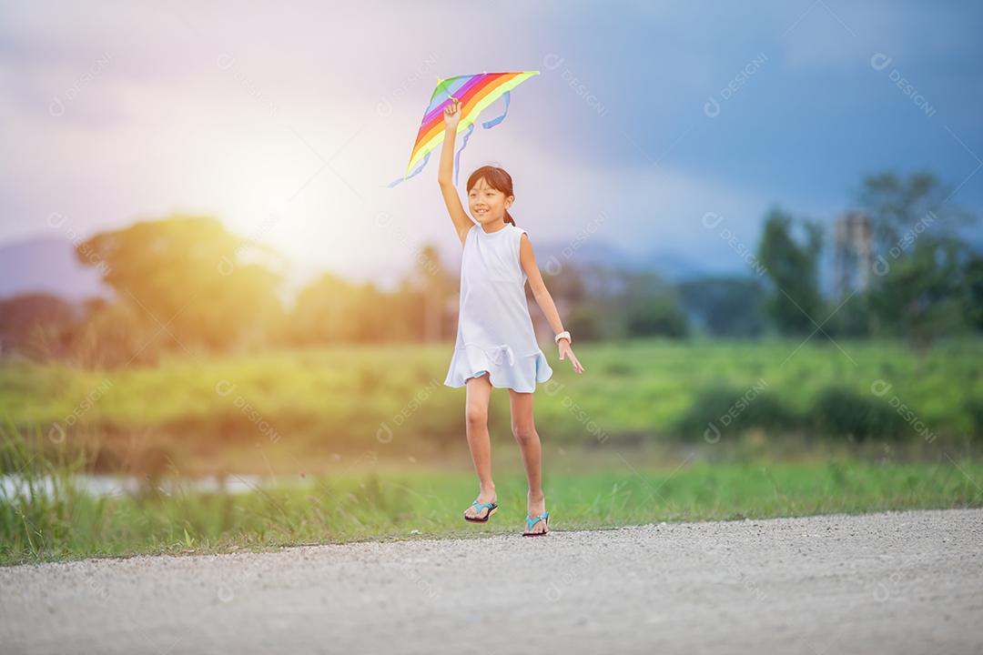 Menina asiática e pai com uma pipa correndo e feliz no prado no verão na natureza