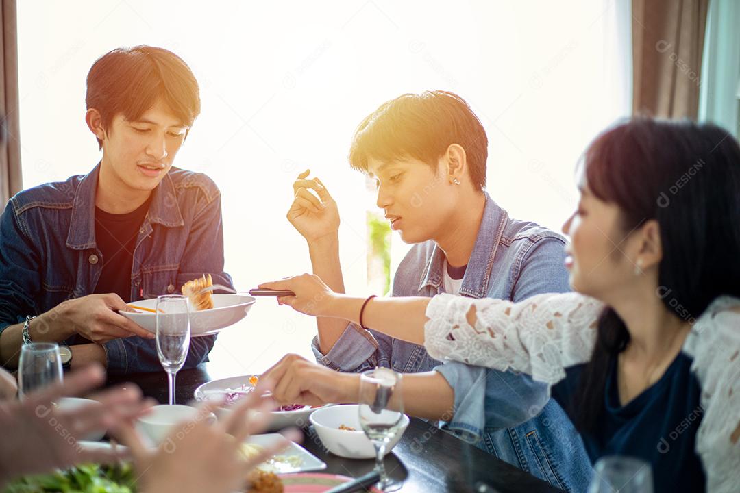 Jantar com o grupo asiático de melhores amigos desfrutando de bebidas à noite enquanto estão sentados à mesa de jantar na cozinha juntos