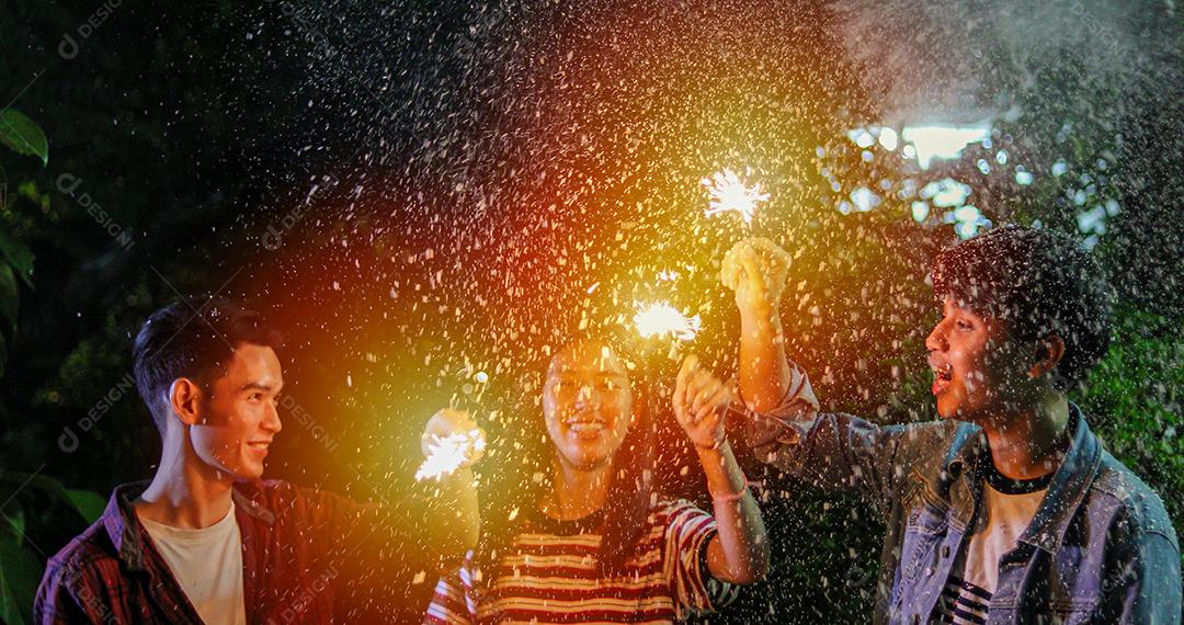 Grupo asiático de amigos fazendo churrasco no jardim ao ar livre rindo com bebidas alcoólicas de cerveja e mostrando grupo de amigos se divertindo com estrelinhas à noite