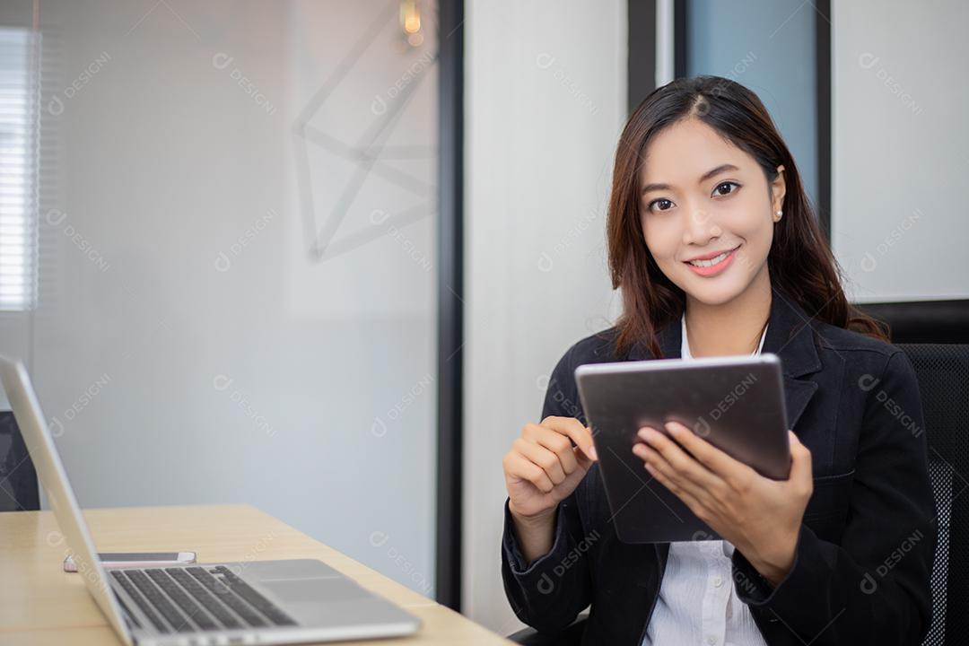 Mulheres de negócios asiáticos usando tablet para trabalhar no escritório relaxam e sorriem