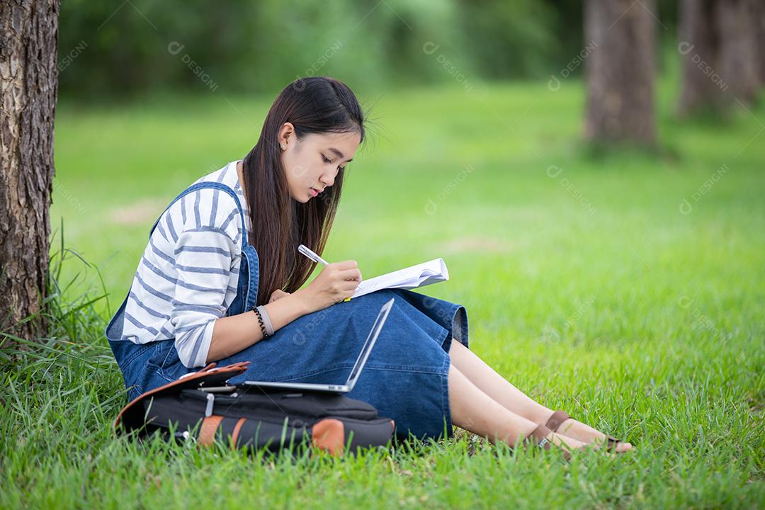 bela estudante asiática segurando livros e sorrindo para a câmera e conceito de aprendizagem e educação no parque no verão para relaxar