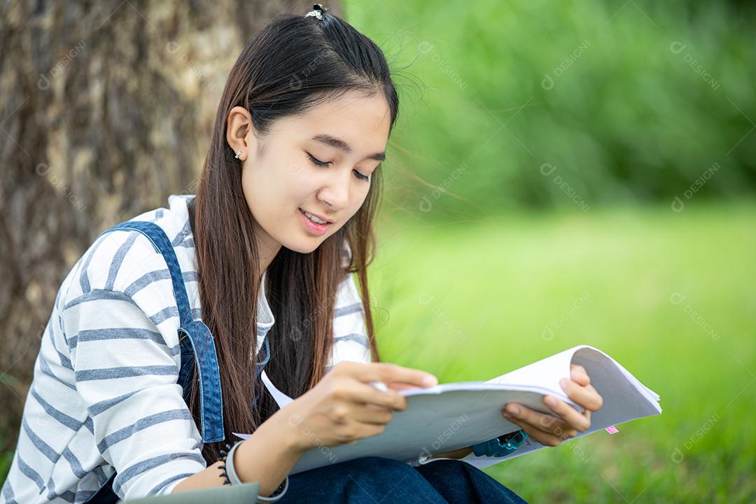 bela estudante asiática segurando livros e sorrindo para a câmera e conceito de aprendizagem e educação no parque no verão para relaxar