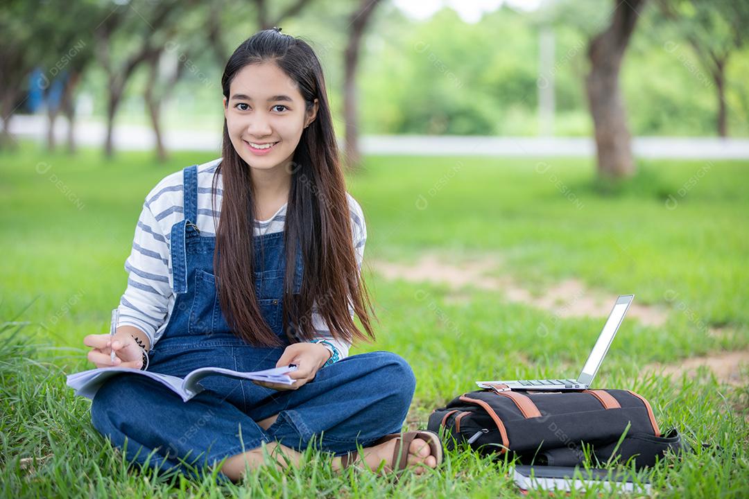 bela estudante asiática segurando livros e sorrindo para a câmera e conceito de aprendizagem e educação no parque no verão para relaxar