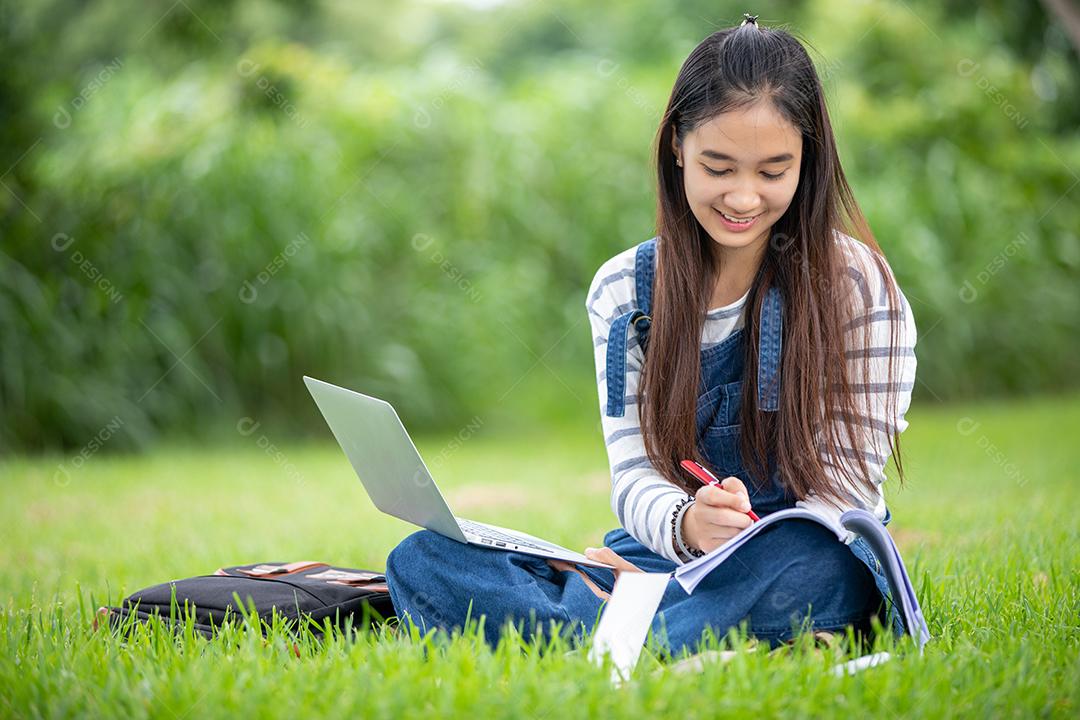 bela estudante asiática segurando livros e sorrindo para a câmera e conceito de aprendizagem e educação no parque no verão para relaxar