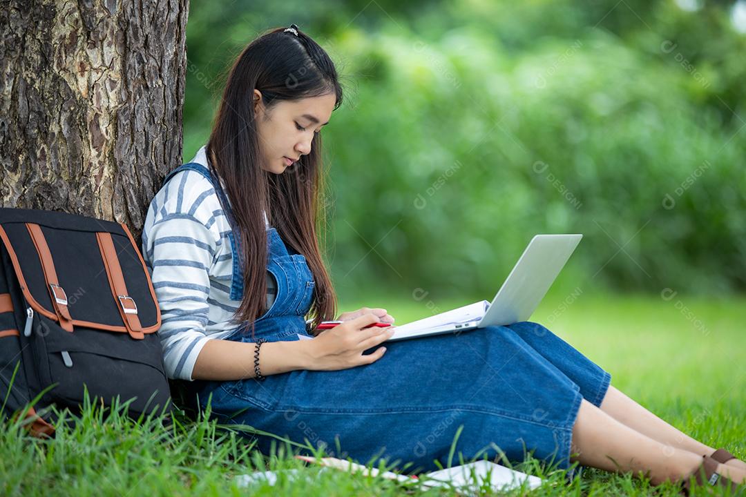 bela estudante asiática segurando livros e sorrindo para a câmera e conceito de aprendizagem e educação no parque no verão para relaxar