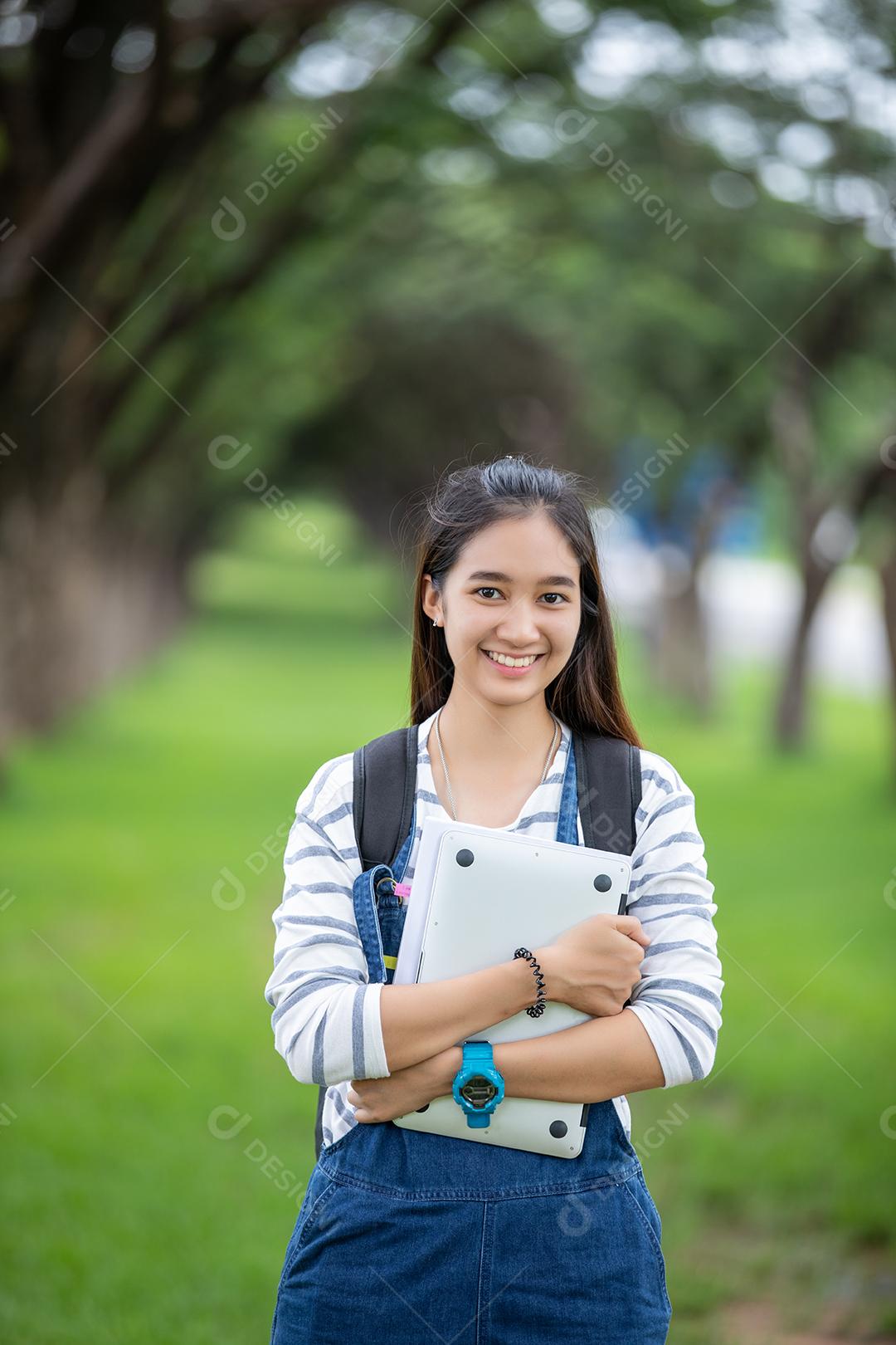 beautiful asian female student holding books and smiling at camera and learning and education concept in park in summer to relax