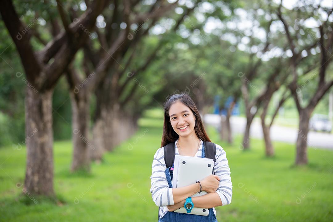 bela estudante asiática segurando livros e sorrindo para a câmera e conceito de aprendizagem e educação no parque no verão para relaxar