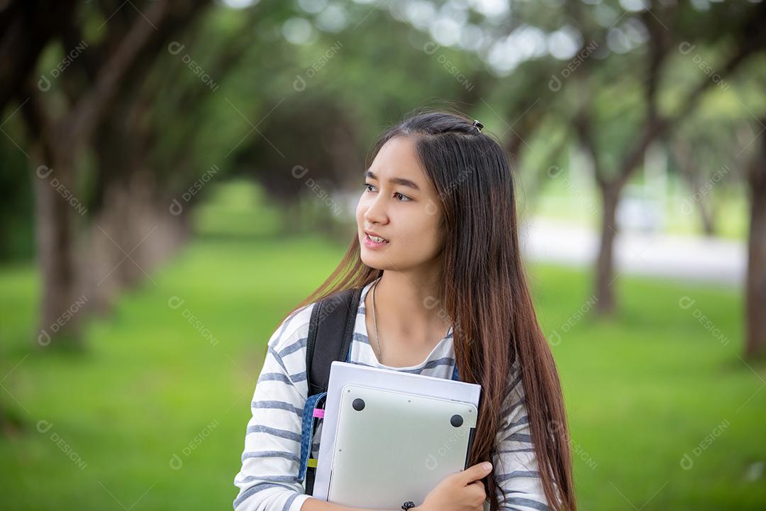bela estudante asiática segurando livros e sorrindo para a câmera e conceito de aprendizagem e educação no parque no verão para relaxar