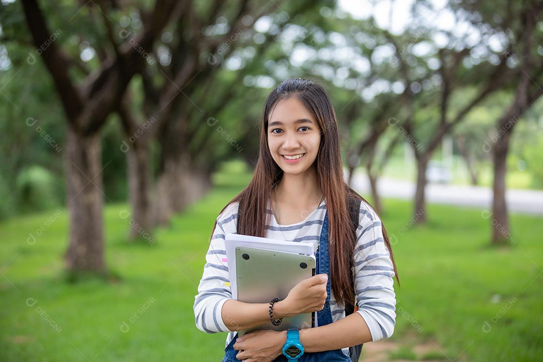 bela estudante asiática segurando livros e sorrindo para a câmera e conceito de aprendizagem e educação no parque no verão para relaxar