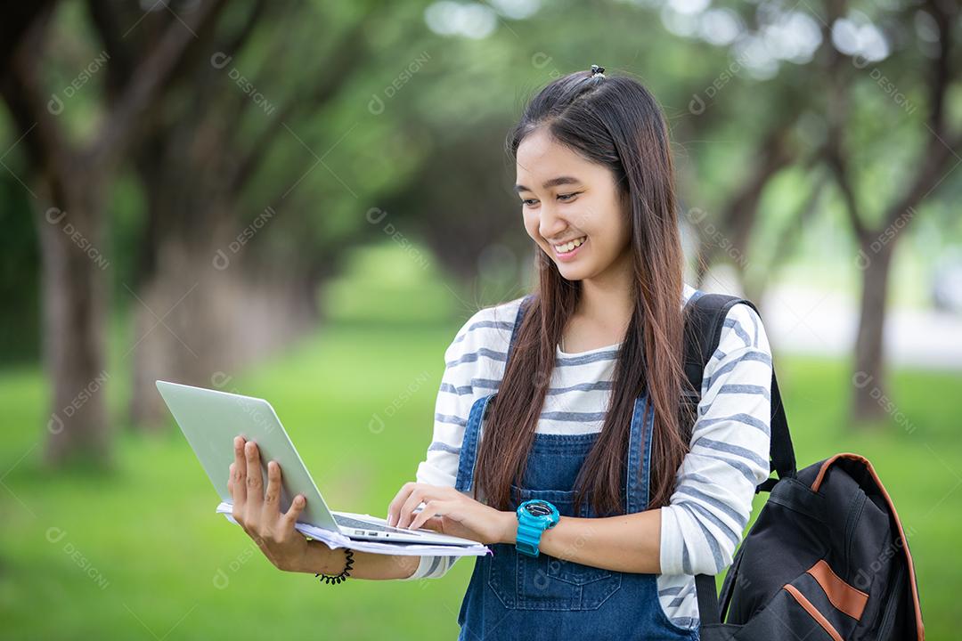 beautiful asian female student holding books and smiling at camera and learning and education concept in park in summer to relax