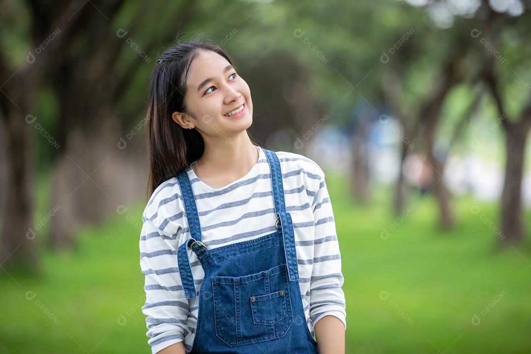 Linda garota asiática sorridente na árvore no parque no verão para relaxar