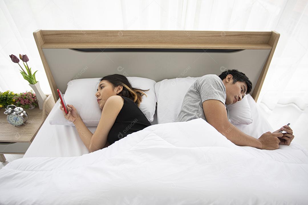 Amantes de casais asiáticos deitados em seus telefones celulares na cama