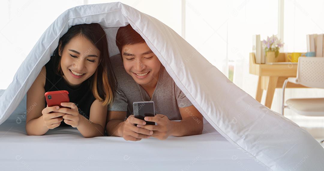 Amantes de casais asiáticos deitados em seus telefones celulares na cama