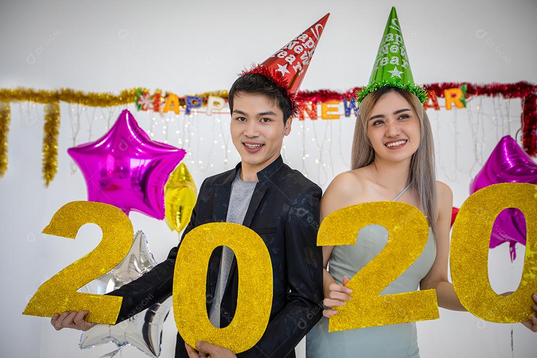 Amante de casal asiático segurando números de 2020 comemorando um ano novo em um bar gritando e rindo e contando até a meia-noite em uma festa de ano novo