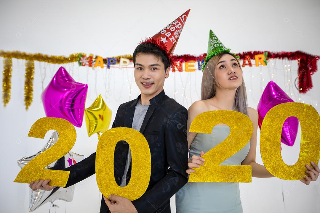 Amante de casal asiático segurando números de 2020 comemorando um ano novo em um bar gritando e rindo e contando até a meia-noite em uma festa de ano novo