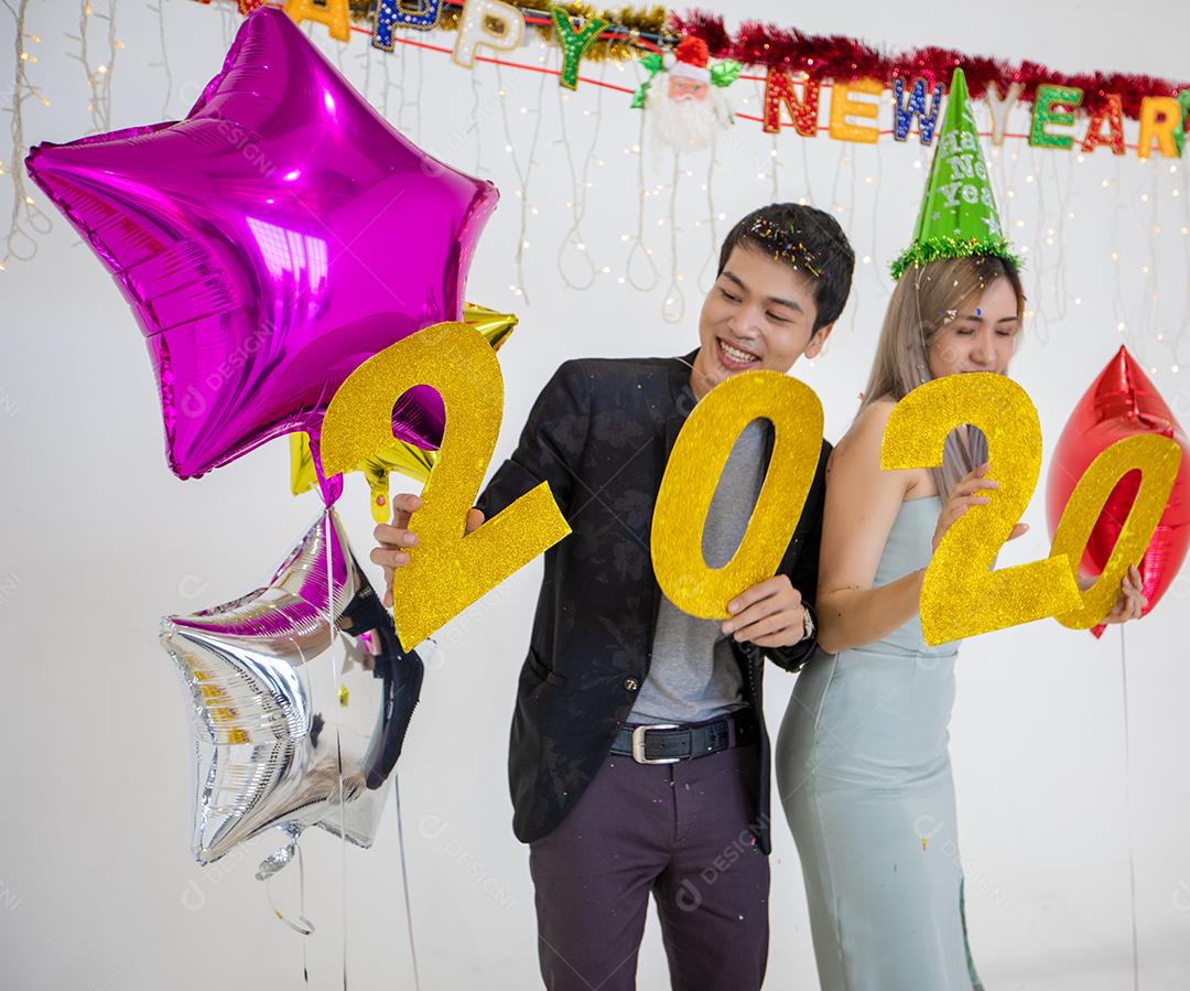 Amante de casal asiático segurando números de 2020 comemorando um ano novo em um bar gritando e rindo e contando até a meia-noite em uma festa de ano novo