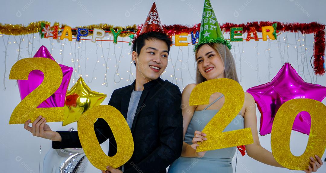Amante de casal asiático segurando números de 2020 comemorando um ano novo em um bar gritando e rindo e contando até a meia-noite em uma festa de ano novo