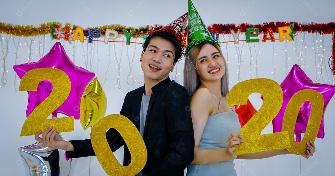 Amante de casal asiático segurando números de 2020 comemorando um ano novo em um bar gritando e rindo e contando até a meia-noite em uma festa de ano novo