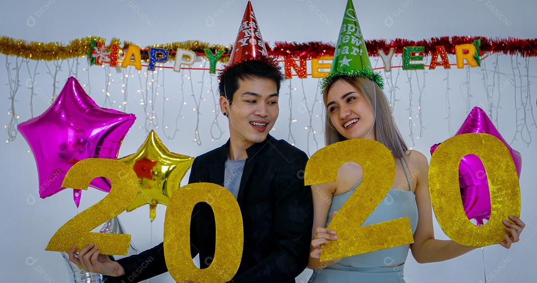 Amante de casal asiático segurando números de 2020 comemorando um ano novo em um bar gritando e rindo e contando até a meia-noite em uma festa de ano novo