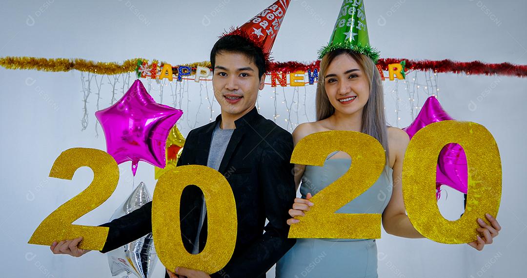 Amante de casal asiático segurando números de 2020 comemorando um ano novo em um bar gritando e rindo e contando até a meia-noite em uma festa de ano novo