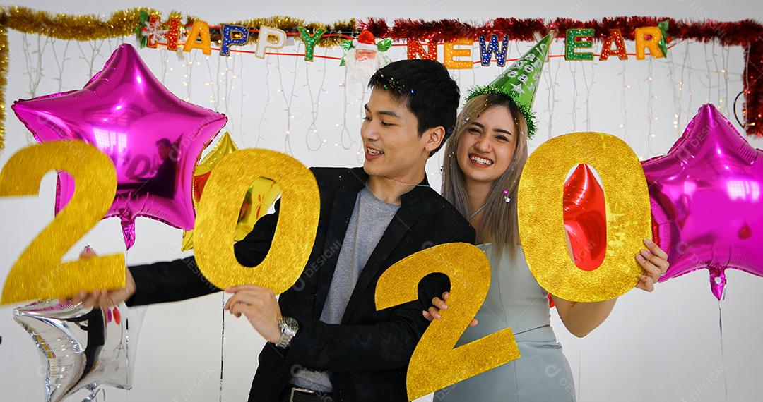 Amante de casal asiático segurando números de 2020 comemorando um ano novo em um bar gritando e rindo e contando até a meia-noite em uma festa de ano novo