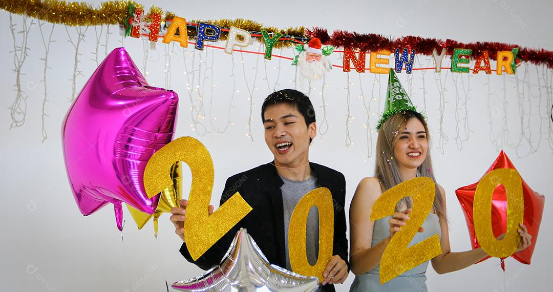 Amante de casal asiático segurando números de 2020 comemorando um ano novo em um bar gritando e rindo e contando até a meia-noite em uma festa de ano novo