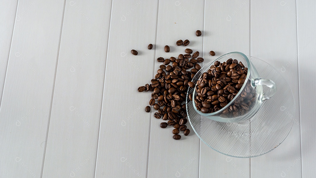 copo de vidro com grãos de café caindo mesa branca