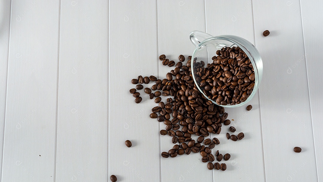 copo de vidro com grãos de café caindo na mesa