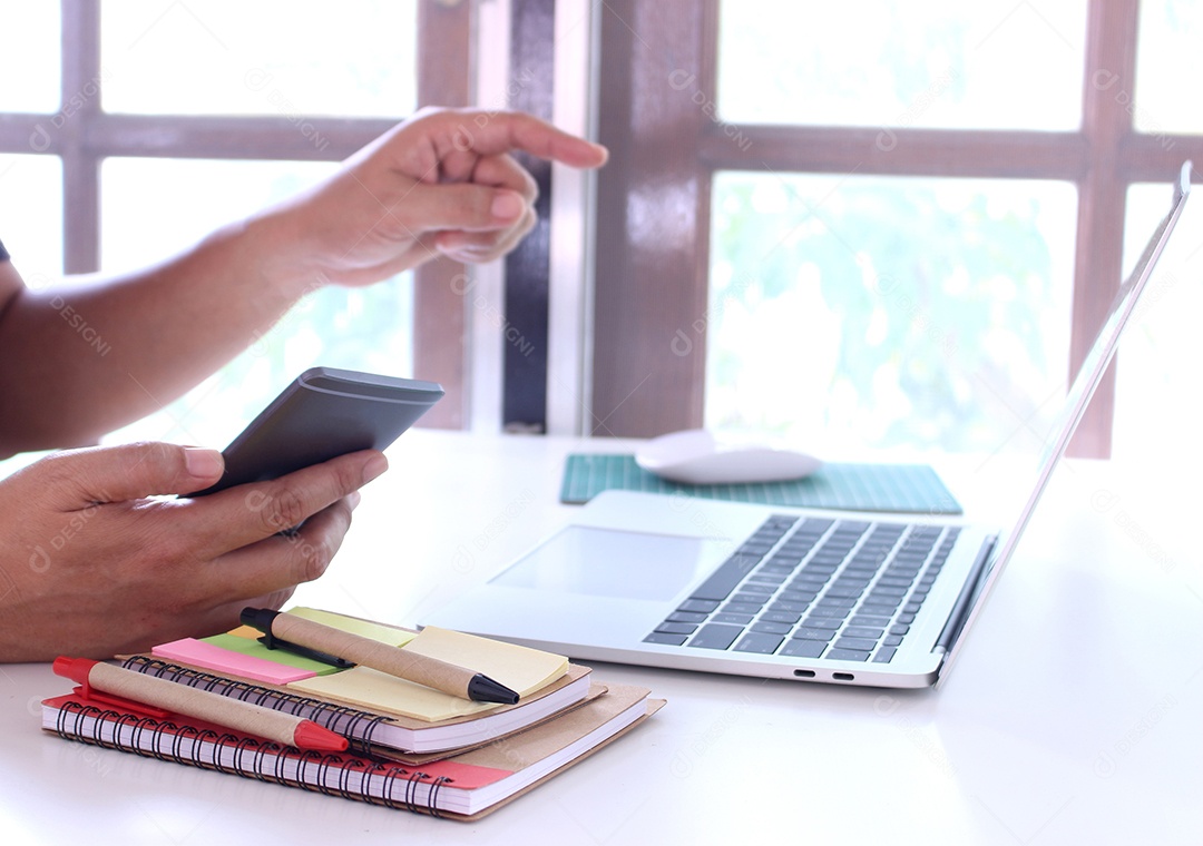 Vista lateral, homem de negócios segurando smartphone e mesa de mesa point.office. espaço de trabalho com notebook e mouse no espaço de cópia