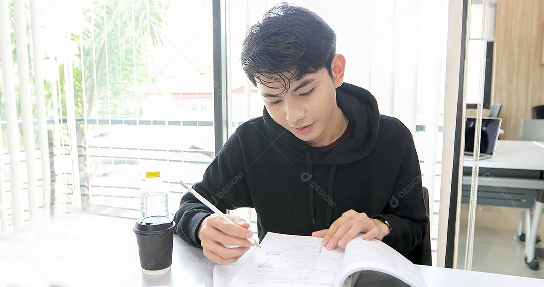 Homem asiático Estudante Sorriem e lendo livro e usando notebook para ajudar a compartilhar ideias no trabalho e projeto. E também revisar o livro antes do exame
