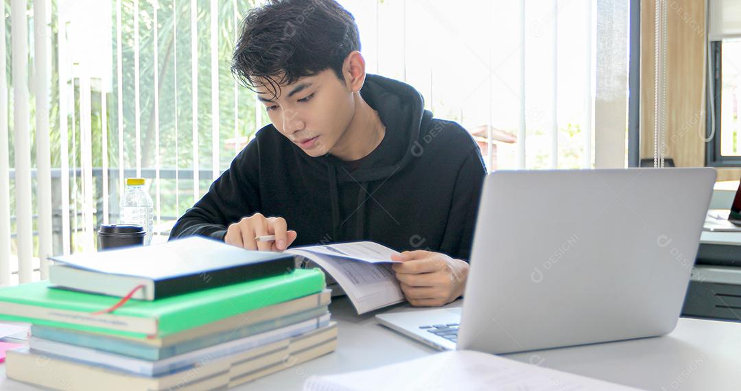 Homem asiático Estudante Sorriem e lendo livro e usando notebook para ajudar a compartilhar ideias no trabalho e projeto. E também revisar o livro antes do exame
