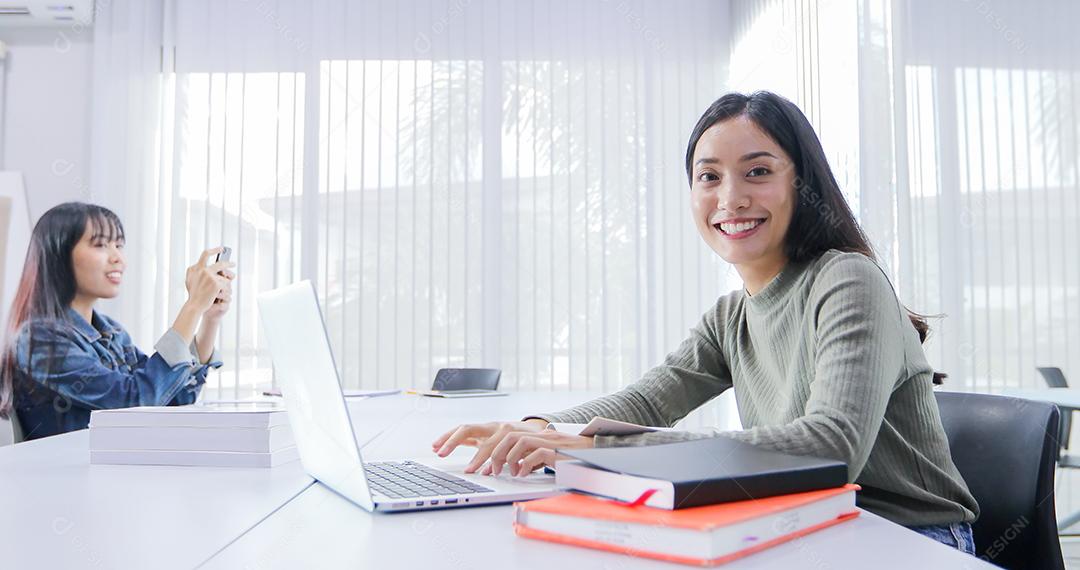 Mulheres asiáticas Estudantes sorriem e lêem livro e usam notebook para ajudar a compartilhar ideias no trabalho e projeto. E também revisar o livro antes do exame