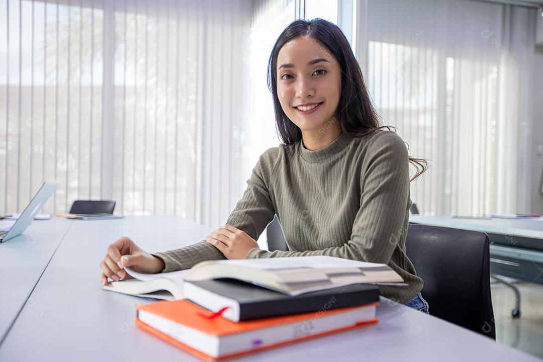 Mulher asiática Estudante sorriem e leem livro e usam notebook para ajudar a compartilhar ideias no trabalho e projeto. E também revisar o livro antes do exame