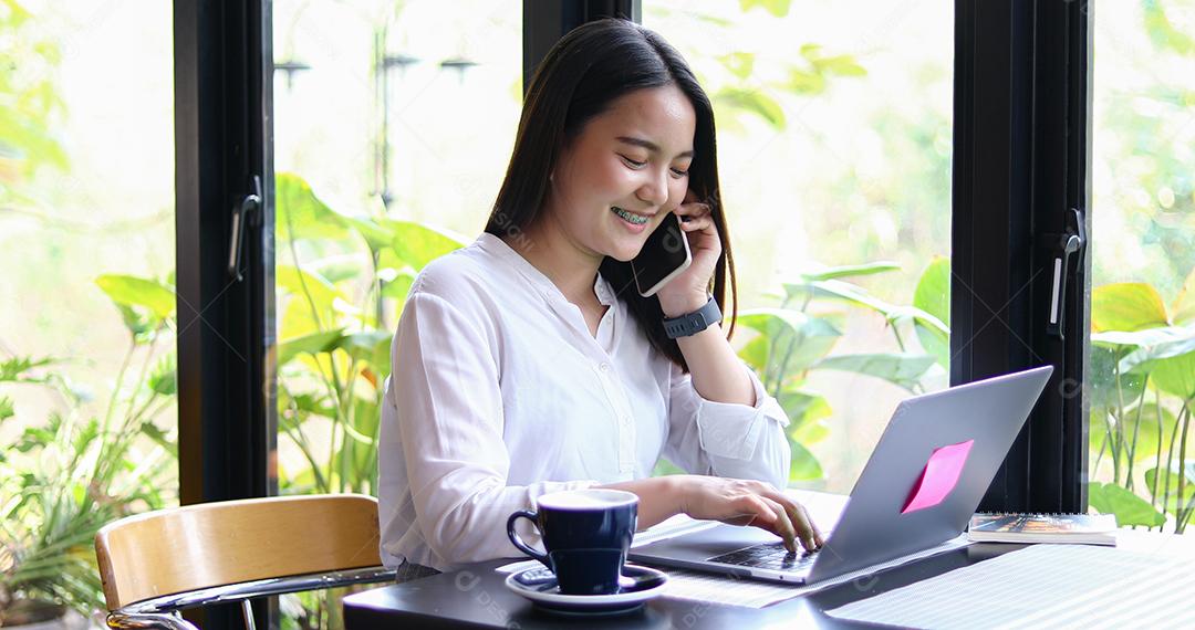 Mulheres de negócios asiáticos estão usando telefone inteligente móvel e sensível ao toque para comunicação e mulheres usando notebook para trabalhar no café