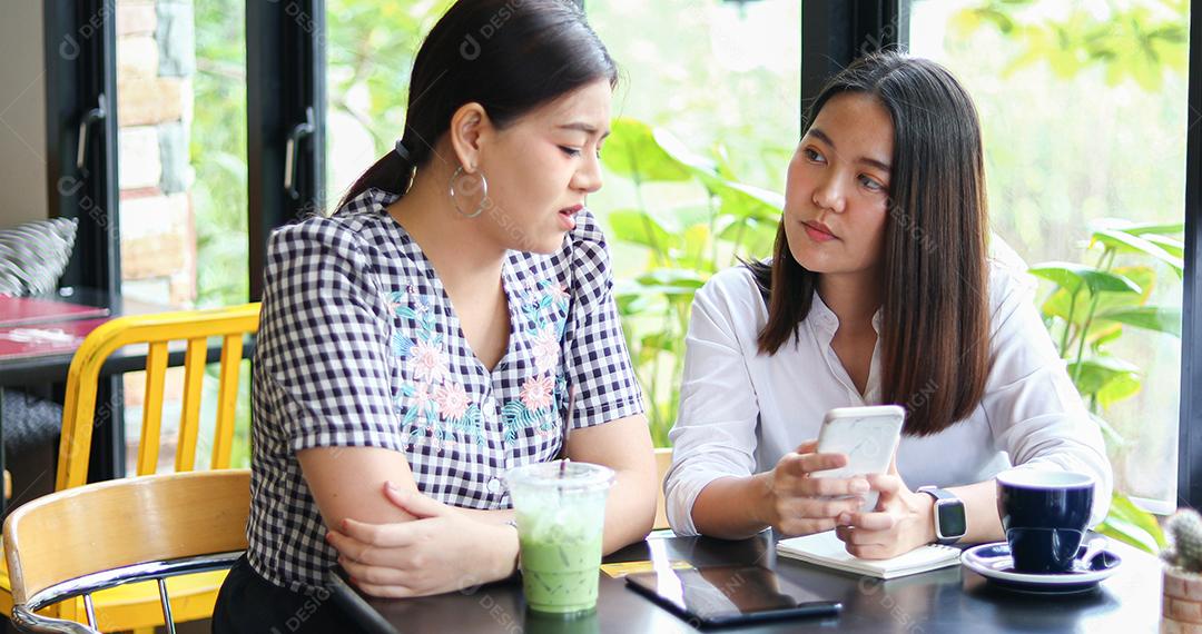 Duas mulheres asiáticas bebendo café em um café e fazendo compras online em telefones inteligentes