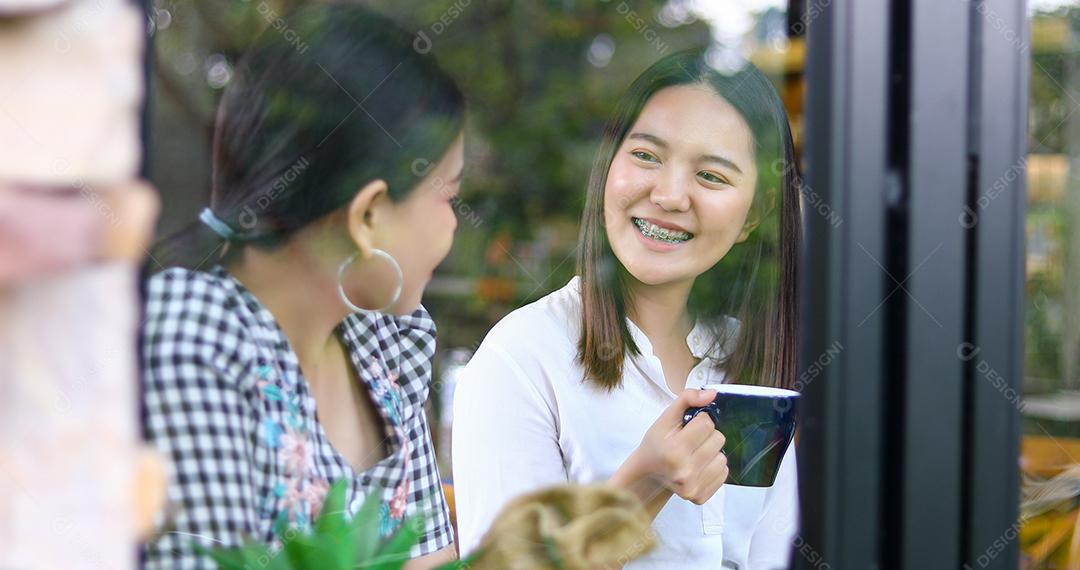 Two Asian women drinking coffee and cheerful women gossiping in a cafe