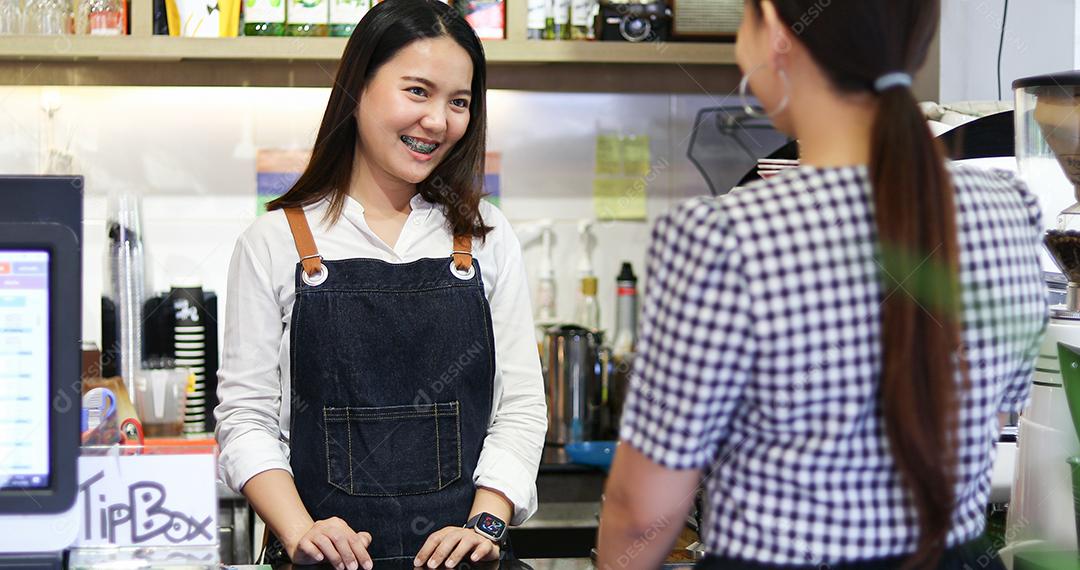 Barista atendendo cliente e mulher está pagando café com cartão de crédito na cafeteria