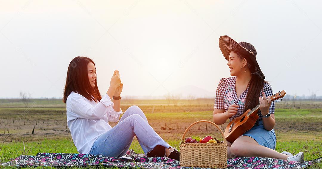 Um grupo de amigos asiáticos jogando Ukelele e passando o tempo fazendo um piquenique nas férias de verão. Eles estão felizes e se divertem nos feriados.