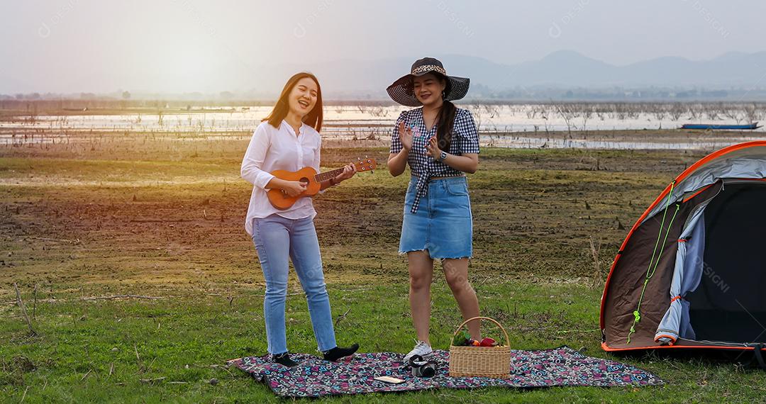 Um grupo de amigos asiáticos jogando Ukelele e passando o tempo fazendo um piquenique nas férias de verão. Eles estão felizes e se divertem nos feriados.