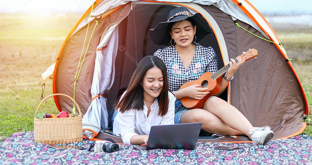 Um grupo de amigos asiáticos jogando Ukelele e passando o tempo fazendo um piquenique nas férias de verão. Eles estão felizes e se divertem nos feriados.