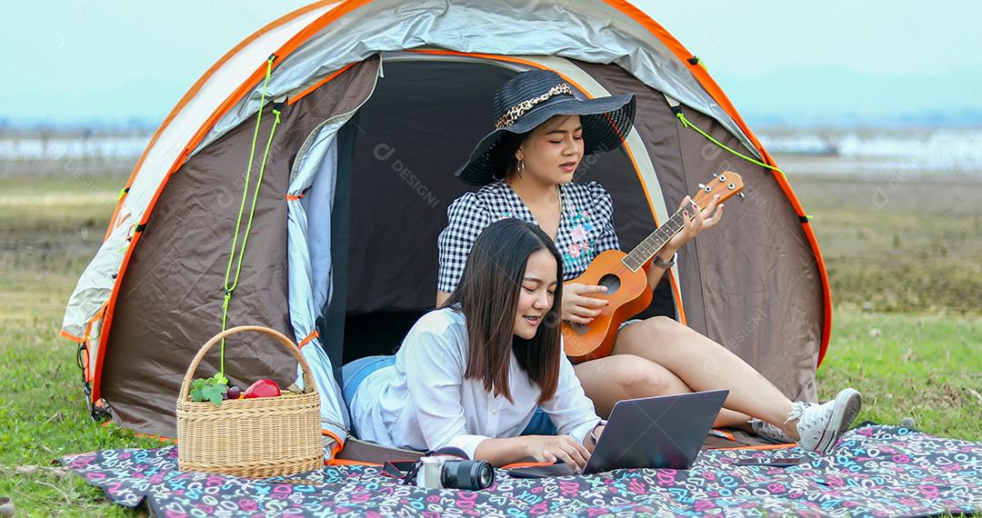 Um grupo de amigos asiáticos jogando Ukelele e passando o tempo fazendo um piquenique nas férias de verão. Eles estão felizes e se divertem nos feriados.