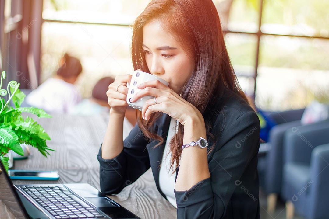 Mulher de negócios asiáticos está trabalhando e bebendo café no café na hora do relaxamento