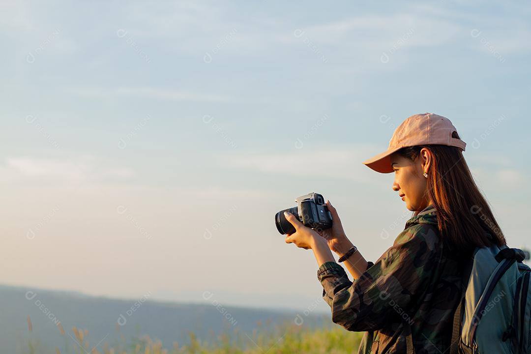 mulheres asiáticas com mochila tirando uma foto à vista no pico da montanha à beira-mar ao nascer do sol