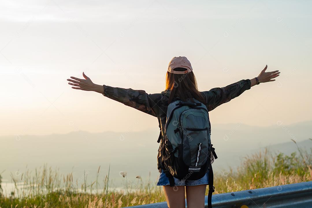 Mulher viajante da liberdade de pé com os braços levantados e desfrutando de uma bela natureza e torcendo o mochileiro jovem no pico da montanha à beira-mar do nascer do sol